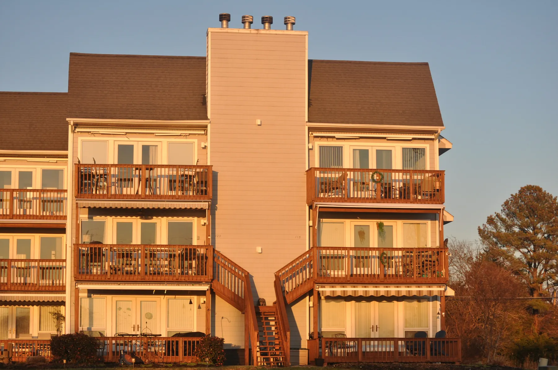 Waterfront townhomes at sunset, shingle roof above tiered wooden balconies