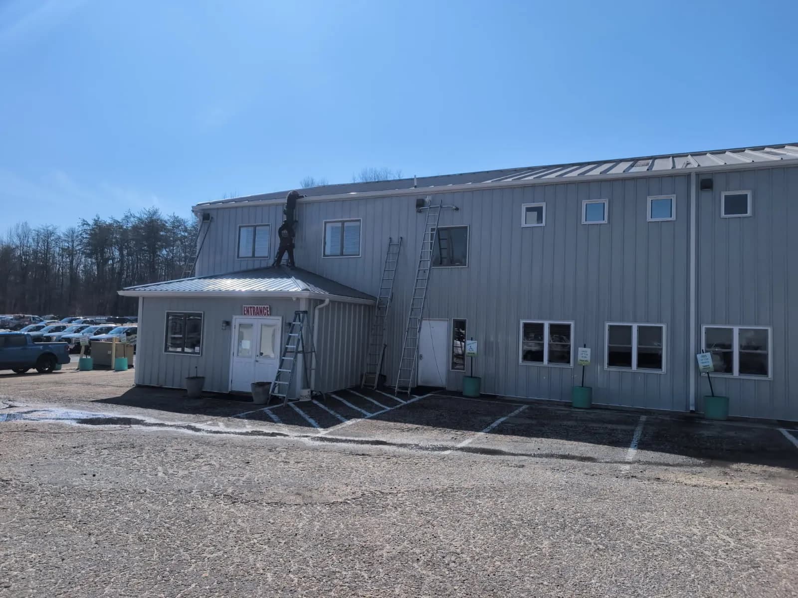 Commercial metal building mid-job, two ladders up and a roofer on the entrance roof